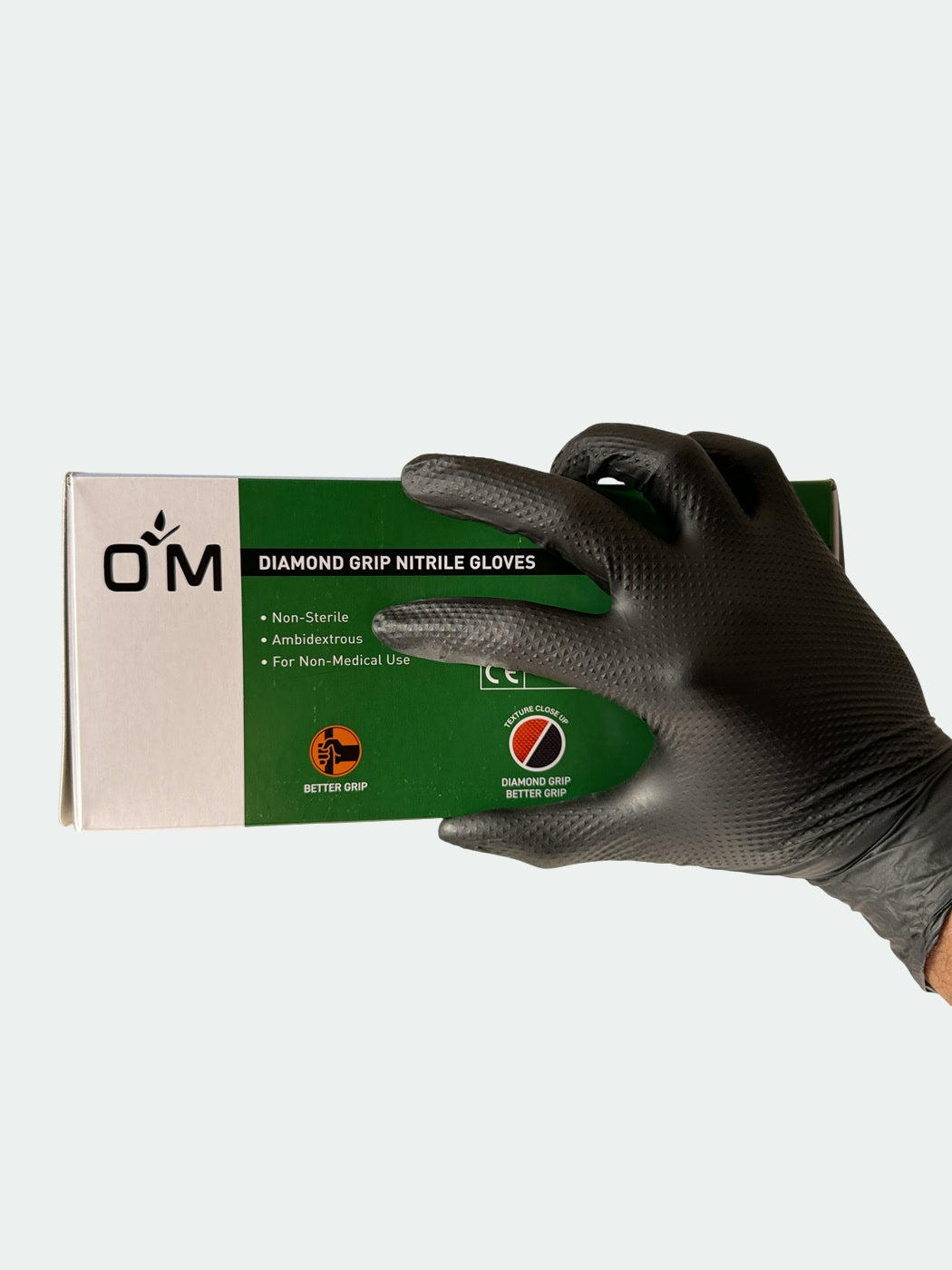 Hand in a black OM Diamond Grip glove holding the OM Diamond Grip Nitrile Gloves box