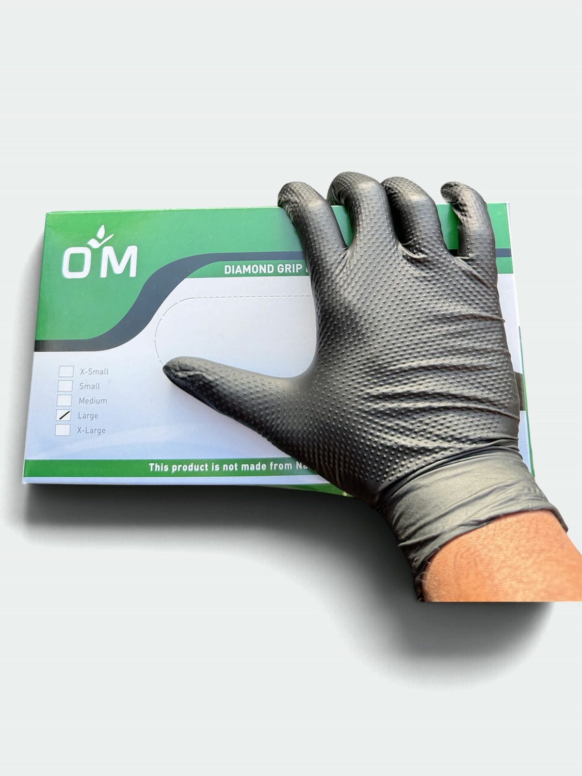 Black OM Diamond Grip glove resting on the OM Diamond Grip Nitrile Gloves box